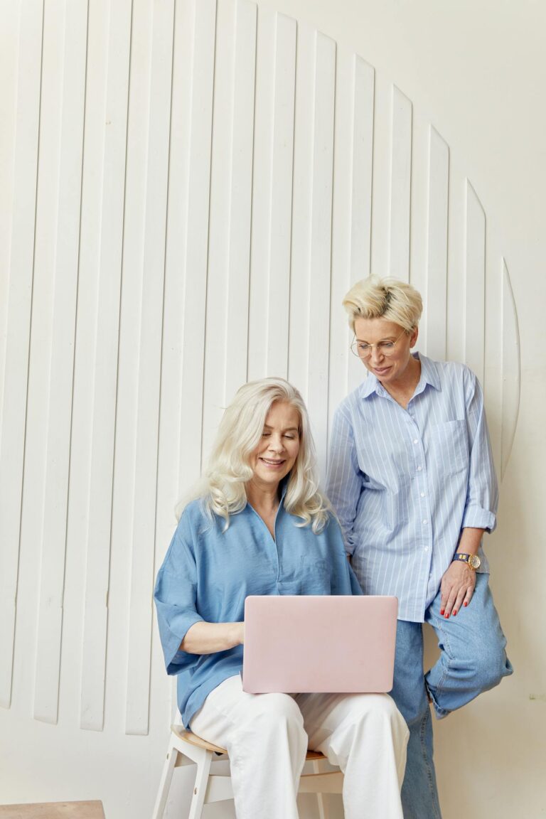 Two diverse businesswomen collaborate on a laptop in a modern office setting, fostering creativity and connection.
